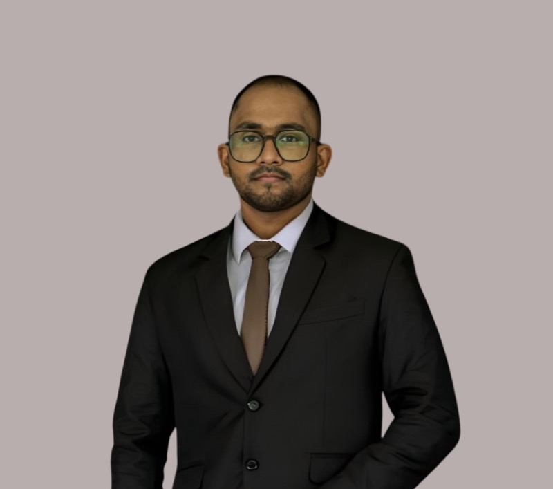 Portrait of Sithija Ranaraja in a dark suit and glasses against a plain grey background.